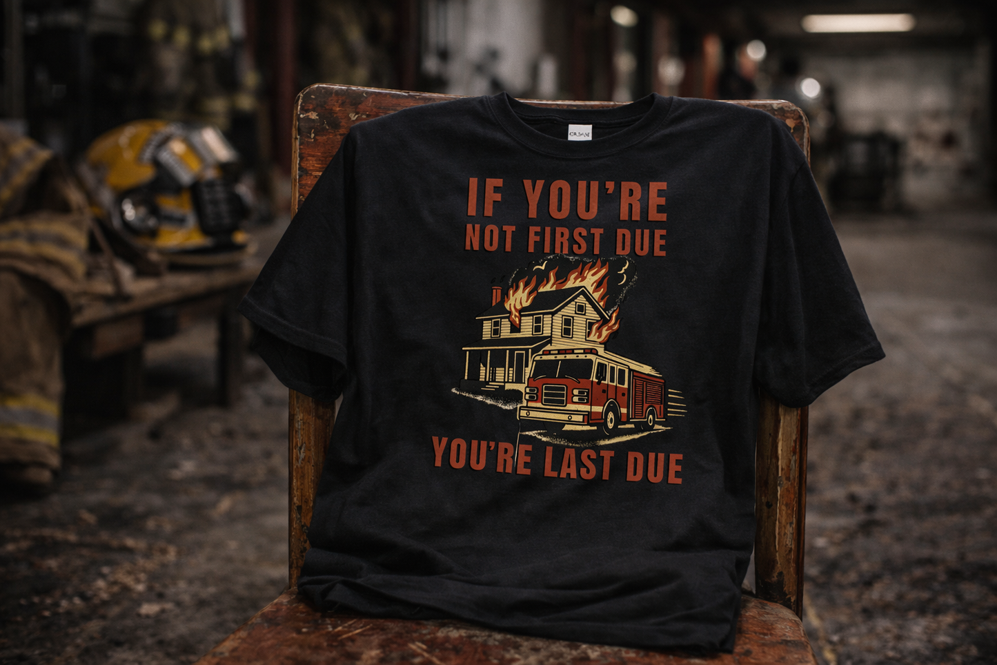 Flat lay of the "First Due or Forgotten" black tee displayed on a chair in a firehouse — Septic & Salty Supply Co. firefighter apparel.