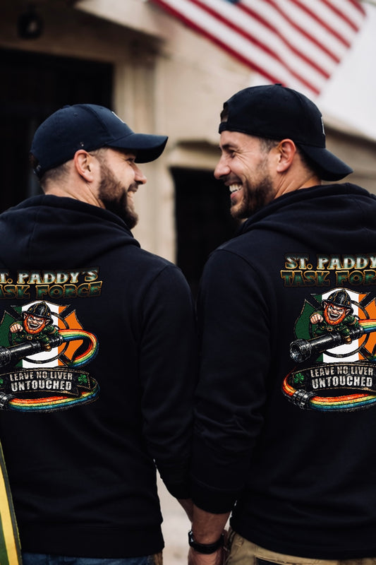 Two firefighters wearing black St. Paddy’s Task Force hoodies standing outside a fire station, showing the back design with Irish leprechaun firefighter graphic and “Leave No Liver Untouched” text.