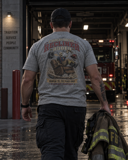 Firefighter walking toward a fire engine while wearing the heather gray Firehouse Recliner Rodeo T-shirt with turnout gear in hand.