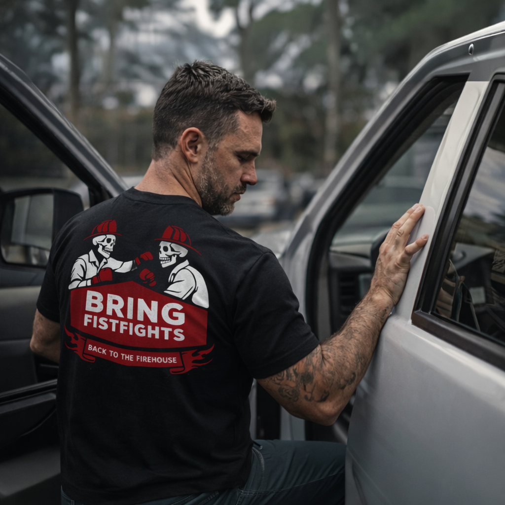 Man wearing the Bring Fistfights Back to the Firehouse black t-shirt, back graphic visible, leaning against a truck door outdoors​​​​​​​​​​​​​​​​