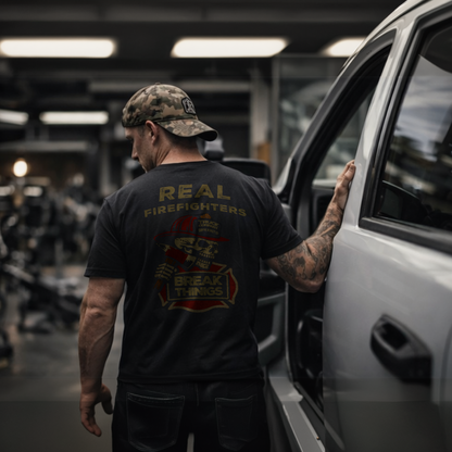 Back view of a firefighter wearing the "Truck Company" black tee featuring the "Real Firefighters Break Things" graphic — lifestyle shot in a vehicle bay with apparatus visible in the background — Septic & Salty Supply Co.